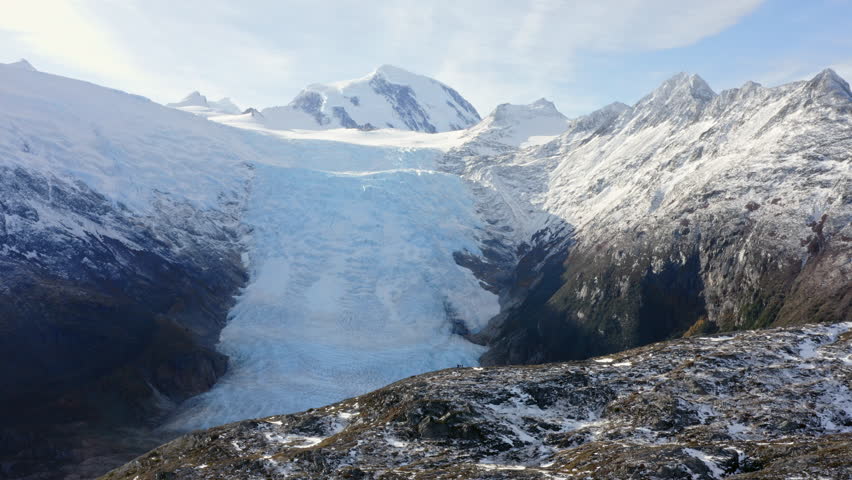 Massive glacier flows between mountain ridges under pale sky in frozen Cape Horn region, aerial tracking reveal left