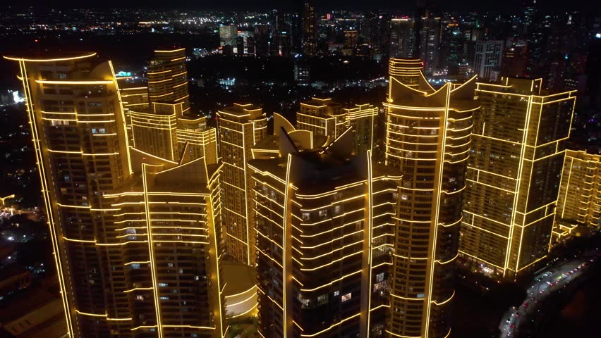 Aerial drone footage of the Rockwell Center skyscrapers in Makati, Metro Manila, glowing with lights at night and surrounded by the vibrant energy of the city skyline.