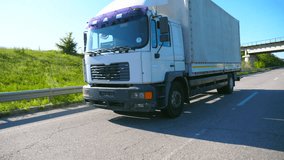 Big truck with cargo trailer driving on highway and transporting goods at sunny day. White lorry riding to destination through countryside road. Transport concept. Slow motion Side view Close up - Powered by Shutterstock - Get 15% off with code: PIKWIZARD15