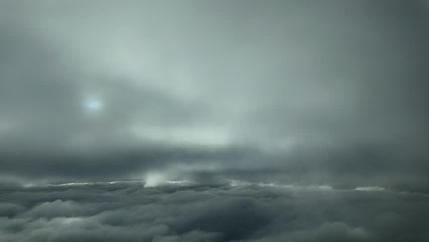 a pilot’s perspective taken from a jet cockpit while flying through layers of darkening clouds with a faded sun veiled by ethereal clouds.