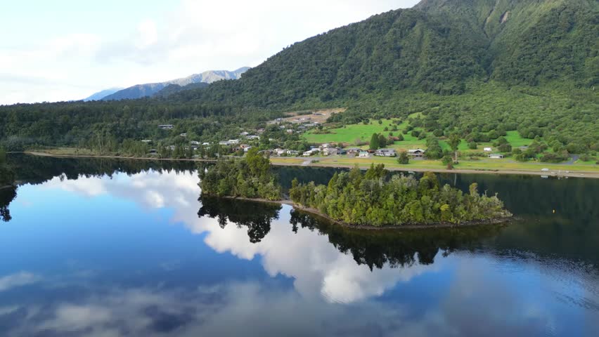 Slow-Motion Drone Flyover of Mirror Lake with Village and Bush-Covered Foothills – New Zealand