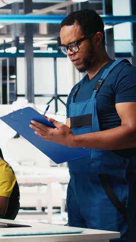 Vertical Video Photovoltaics factory supervisor reviews industrial guidelines of solar plant production, robot arms placing solar panels on conveyor belts. Man reads inspection machinery parameters