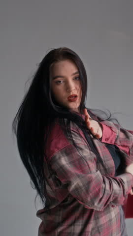 Vertical shot of female Caucasian zoomer in plaid shirt dancing on camera in minimalist studio