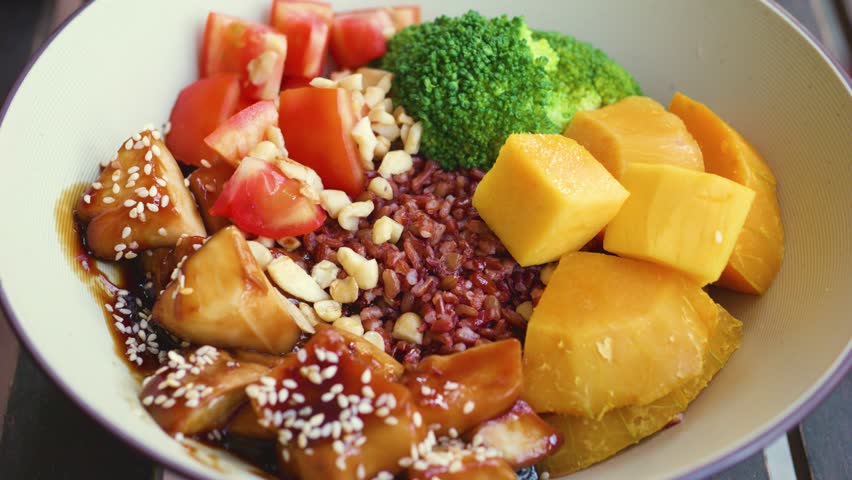 Colorful plant based plate featuring rice, meat alternative, roasted vegetables, mango, accompanied by creamy avocado pudding sprinkled with mixed seeds, nuts, dried fruit