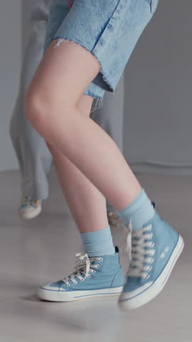 Vertical cropped shot of legs of anonymous dancers performing hip hop moves in modern studio during rehearsal