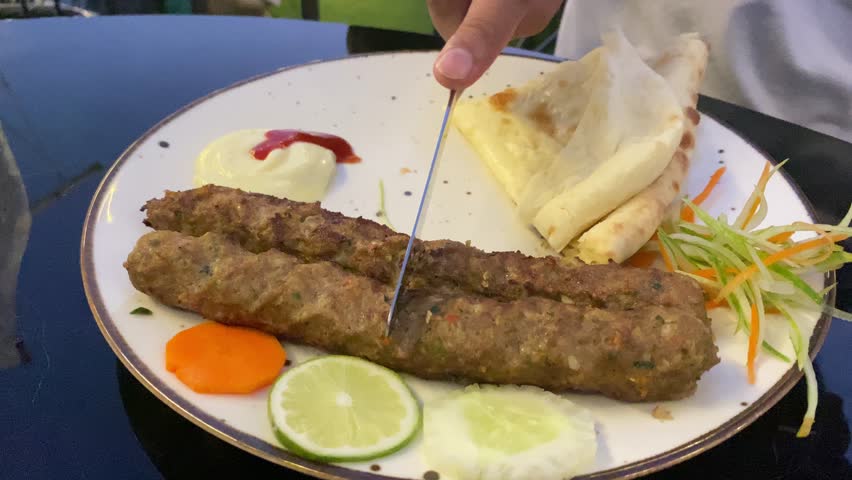 Hand cutting delicious popular Indian kebab with silver knife with soft naan roti flatbread