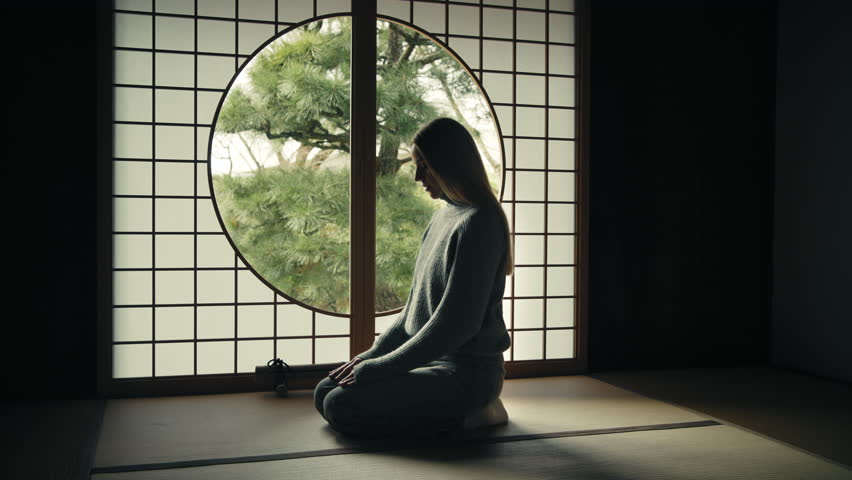 Beautiful caucasian woman sitting in seiza position and meditating in a traditional Japanese house with a circular window