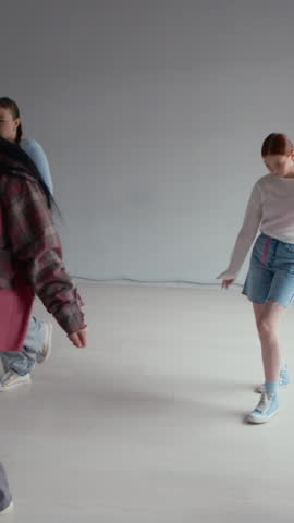 Vertical shot of Caucasian girls in streetwear practicing hip hop moves during rehearsal in studio