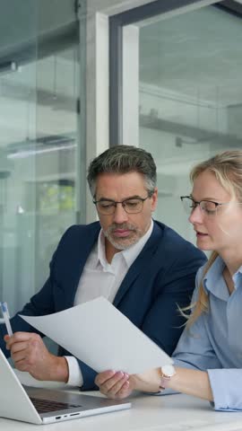 Team of partners mature man and young woman discussing financial banking document report sitting at table in office. Two colleagues professional business people working together on project. Vertical