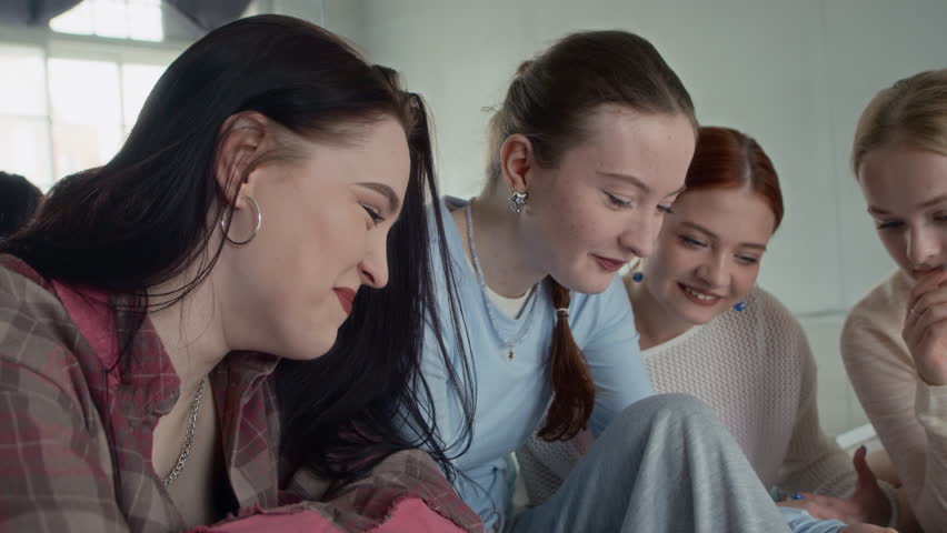Handheld shot of four Caucasian gen Z girls in streetwear reviewing their dance filmed on smartphone in studio