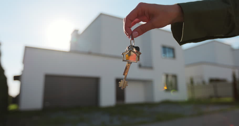 A hand with a keychain in the shape of a small house and keys against the background of house.