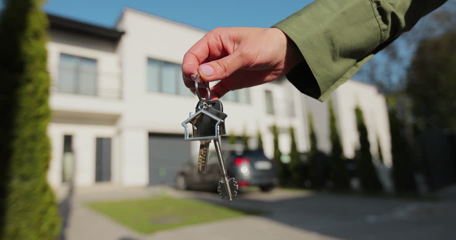 Key ring with keychain house in hand on background of house. Real estate concept for buying a new home.