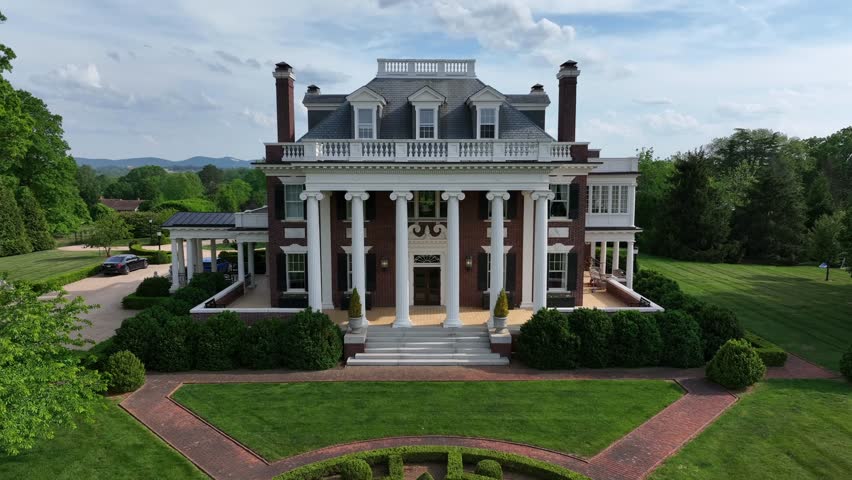 Aerial backwards wide shot of luxury mansion villa during sunny day. Spring trees in quiet american suburb. Lynchburg, Virginia. Neat well-kept garden with green grass.