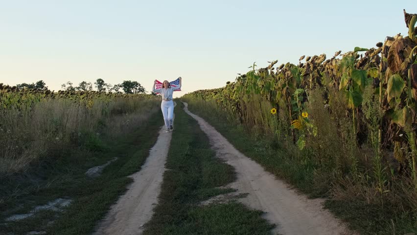Young woman running with Waving American Flag on field Background. Flag of the united states of America. July 4th Independence Day. USA patriotism national holiday proud