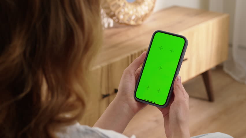 Woman sit use digital tech cell phone open green screen mock up. Hand scroll iphone web site swipe unlock. Girl hold mobile closeup. Turn on chroma key page Cozy home background. Online app copy space