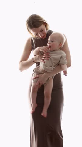 Young stylish mom in brown dress dancing with child in bright room. Joyful bonding, happy family, mother and baby