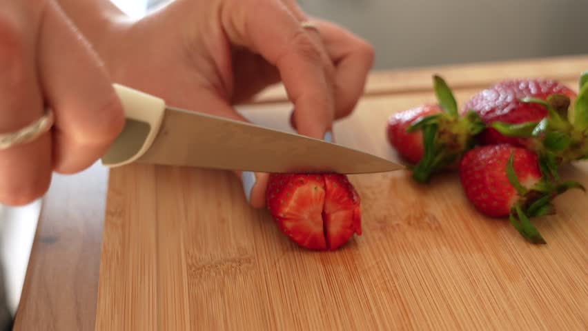 Female hands chopping strawberries with knife on wooden board