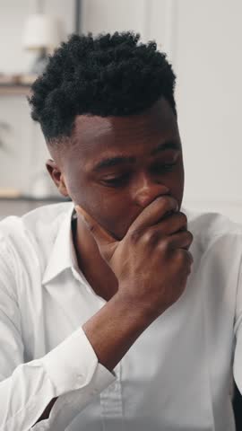 Portrait of bored african american man in room, vertical video, psychological problems. Emotional black male person thinking about troubles, startup owner or young businessman dreaming about money