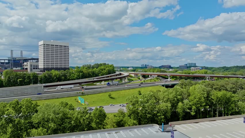 Traffic scene with trucks and cars in american suburb. Overpass highway with green trees and clouds at sky. Aerial wide shot. Office complex block in Atlanta, Georgia.