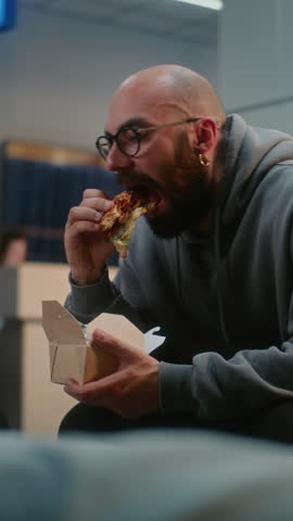 Crowded International Airport Terminal: Man Eating Fast Food Sitting in Departure Lounge. Diverse Passengers and Travelers Waiting for Delayed Airplane Flight, Going on Holiday Trips. Vertical Shot.
