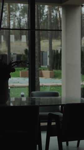 Dining area with a table and a stylish vase in front of the window in silhouette. View of the street .Vertical video