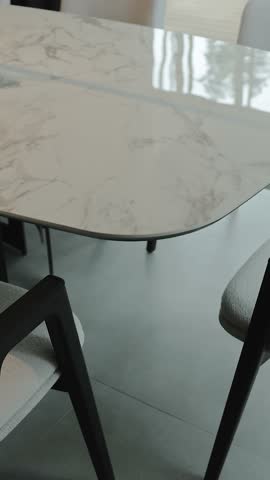 Close-up of a marble dining table combined with modern chairs, located in a bright living room. Vertical video