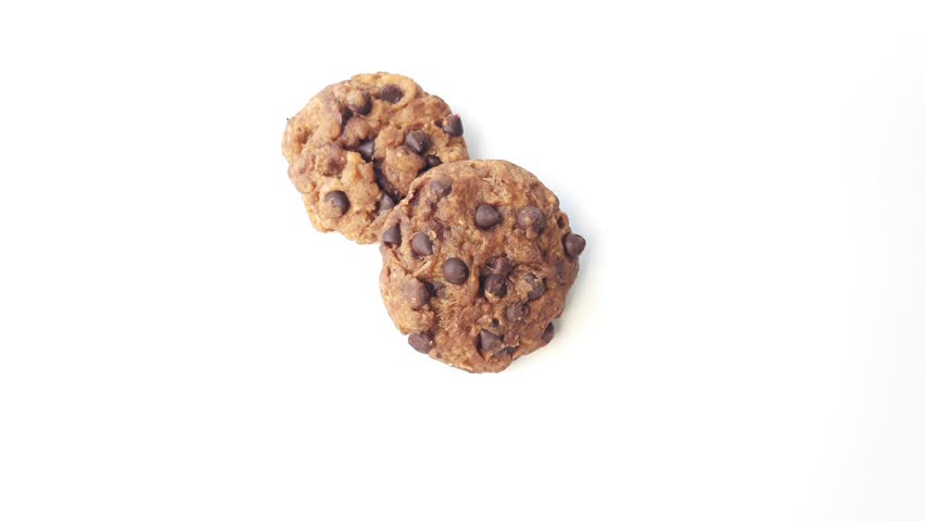 footage of two dark chocolate chip soft cookies on a white bakcground surface one of which is taken. top view,flat lay,horizontal
