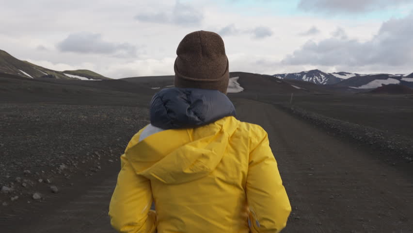Beautiful young asian woman in yellow jacket running on ground road among volcano wilderness in Icelandic Highlands on summer at Iceland