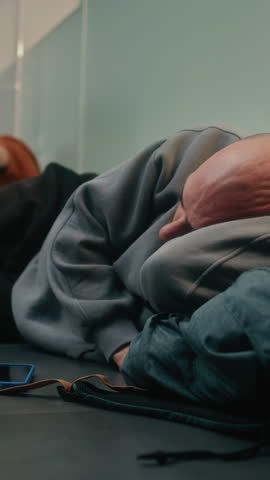 Crowded International Airport Terminal: Exhausted Man Sleeping on the Floor in Departure Lounge. Diverse People and Passengers Waiting for Delayed Airplane Flight. Tourism and Travel. Vertical Shot.
