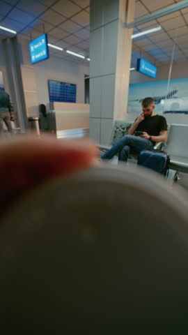 Crowded Airport Terminal: POV Passenger Sitting in Boarding Lounge of Airline Hub, Drinking Coffee from Paper Cup. Tourists Waiting for Flight, Going on Holiday Trips. First-Person View. Vertical Shot