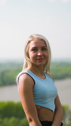 Pretty woman turns head and smiles to beloved man motorcyclist at romantic date on hilly bank of large river on sunny spring day slow motion