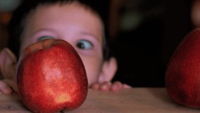 A close-up shot showing a child's eyes and forehead peeking over the edge of a wooden table. In the foreground, two red apples sit on the table - Powered by Shutterstock - Get 15% off with code: PIKWIZARD15
