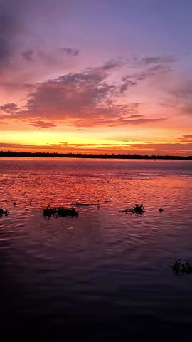 A mesmerizing twilight scene featuring a tranquil body of water reflecting the vibrant hues of the setting sun. Rio Magdalena, Barranquilla, Colombia