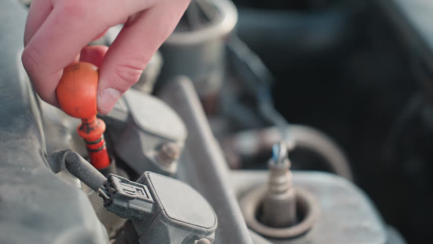Close up of car engine with red dipstick being returned after checking oil level, hand partially visible in frame during cold weather maintenance routine with mechanical parts