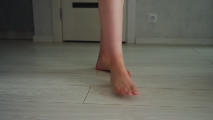 Close up leg view of woman walking across light wood floor inside modern living space barefoot steps showing calf and foot movement towards sofa area near doorway in bright minimalist interior