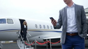 Businessman checking smartphone near jet by rope barrier on tarmac, with animated status chart. Luxury, professionalism, travel, corporate, elite, modern, sleek - Powered by Shutterstock - Get 15% off with code: PIKWIZARD15