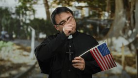 Young man dressed as priest holding american flag in a park setting, blending religious symbolism with national identity in an outdoor environment. - Powered by Shutterstock - Get 15% off with code: PIKWIZARD15
