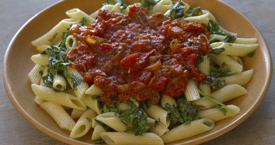 Penne pasta with arugula leaves and tomato sauce with celery. Simple, healthy vegan food. Table spin.