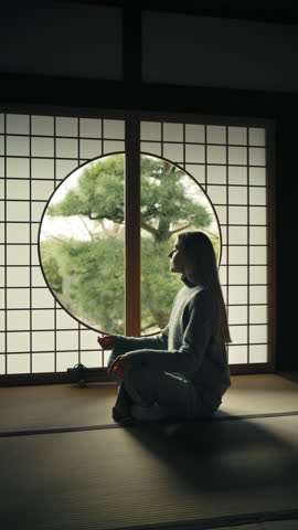 Young and beautiful caucasian woman sitting on her knees and meditating inside a traditional japanese home
