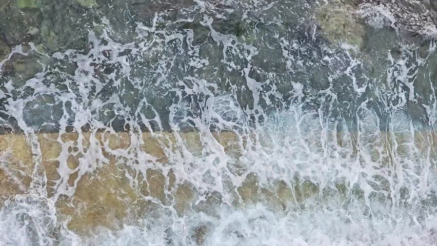 Soft seawater washing against concrete dock, generating rhythmic patterns with gentle blue waves and white foam, creating tranquil maritime scenery during sunny daytime