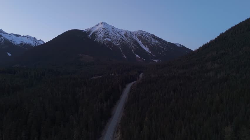 Aerial View of Winding Dirt Road Amidst Mountain Forest at Dawn in British Columbia
