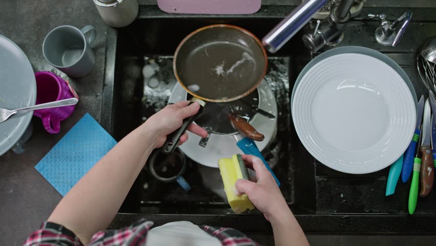 Close-up of female hands washing dishes in the sink with a sponge.