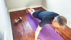 A fit, slim man performs press-ups at home in a bright, uncluttered spare room. Dressed in short shorts and a tight workout top, he exercises on a simple mat with a pair of dumbbells visible nearby.  - Powered by Shutterstock - Get 15% off with code: PIKWIZARD15