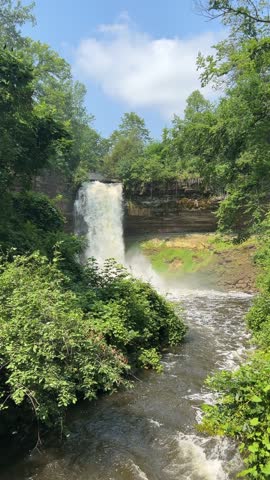 Minnehaha Falls plunges into a creek surrounded by green summer foliage