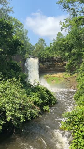 Minnehaha Falls plunges into a creek surrounded by green summer foliage
