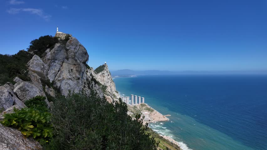 Panoramic view of Gibraltar rock with vegetation overlooking modern buildings and the Mediterranean sea under a clear blue sky