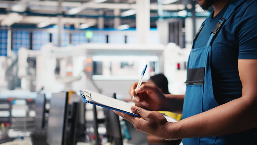 Black photovoltaics factory specialist checking configuration files, analyzing data to ensure seamless production. Solar panels manufacturing plant employee reading user manual. Camera B.