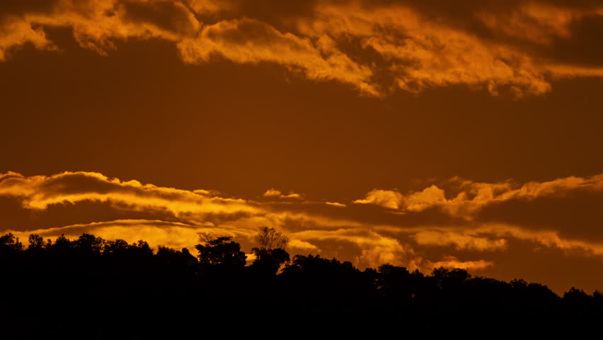 Time lapse of the sun rising over hills that are covered with clouds, in the style of smokey background.