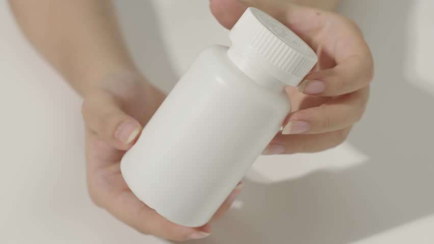 Close-up of hand holding the cap of a dietary supplement bottle and rotating to open it. After opening the bottle, the hand takes the cap out. The bottle has no label, used for product advertising.