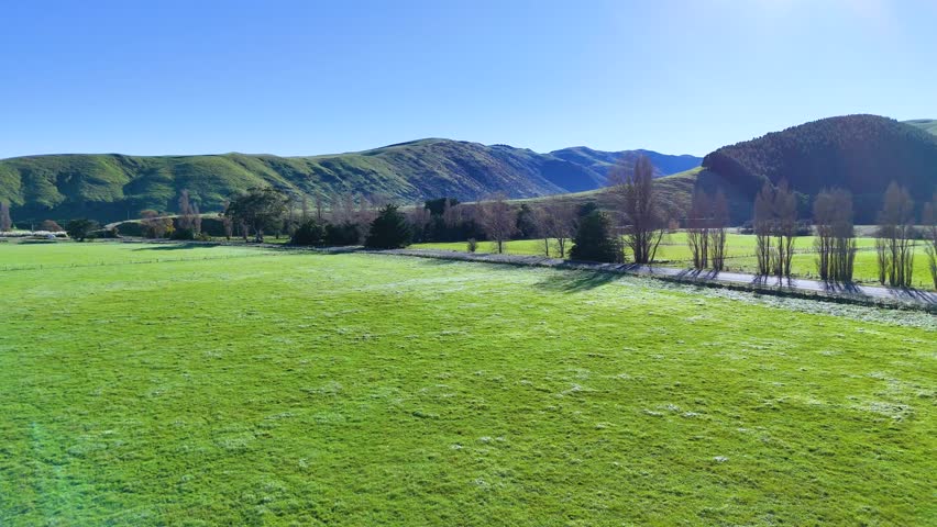 Aerial view of lush green fields and distant hills under clear blue skies in Akaroa, New Zealand